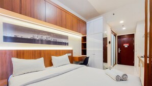 Ein Hotelzimmer mit einem ordentlich bezogenen Bett, einem hölzernen Kopfteil, einem Schreibtisch mit Stuhl und einem Kleiderschrank.