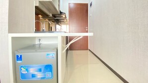 A narrow hallway with a kitchen area on the left, a door on the right, and a water dispenser in the center. - Cozy Studio Apartment At Gateway Pasteur (Cimahi)