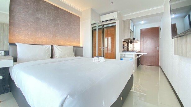 A modern hotel room with a large bed, a desk with a chair, a built-in TV, and a wardrobe. - Cozy Studio Apartment At Gateway Pasteur (Cimahi)