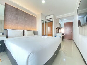 A modern hotel room with a large bed, a desk with a chair, a built-in TV, and a wardrobe. - Cozy Studio Apartment At Gateway Pasteur (Cimahi)