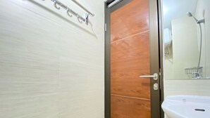 A bathroom with a wooden door, a white sink, and a mirror. - Cozy Studio Apartment At Gateway Pasteur (Cimahi)