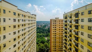 A high-rise residential building with multiple balconies, a clear view of a cityscape, and a lush green area in the background. - Cozy And Warm 2Br At Kebagusan City Apartment (Jakarta)