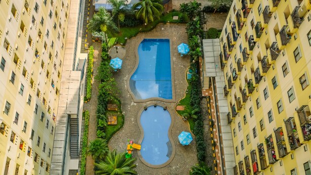 A residential building with a central swimming pool surrounded by greenery and outdoor seating. - Cozy And Warm 2Br At Kebagusan City Apartment (Jakarta)