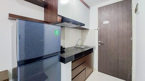 A compact kitchen with a stainless steel refrigerator, a sink, and wooden cabinets. - Fancy And Nice Studio Apartment At Serpong Garden (Cisauk)