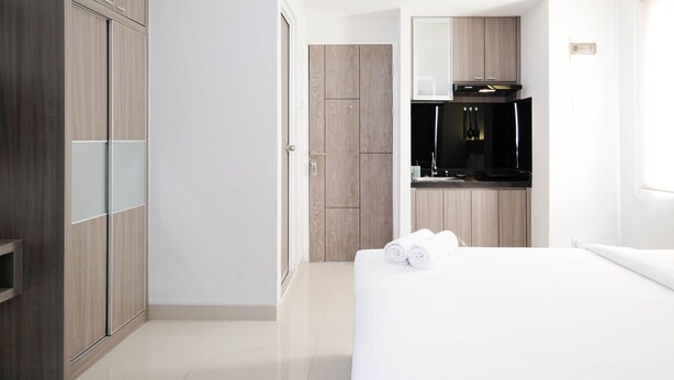A hotel room with a bed, a wardrobe, a bathroom with a mirror, and a kitchenette. - Cozy Living Studio At Taman Melati Surabaya Apartment (Surabaya)