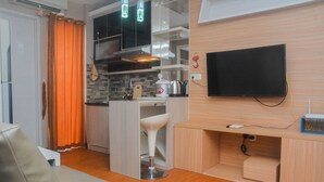 A compact living space with a kitchenette, a flat-screen TV mounted on the wall, and a small seating area.