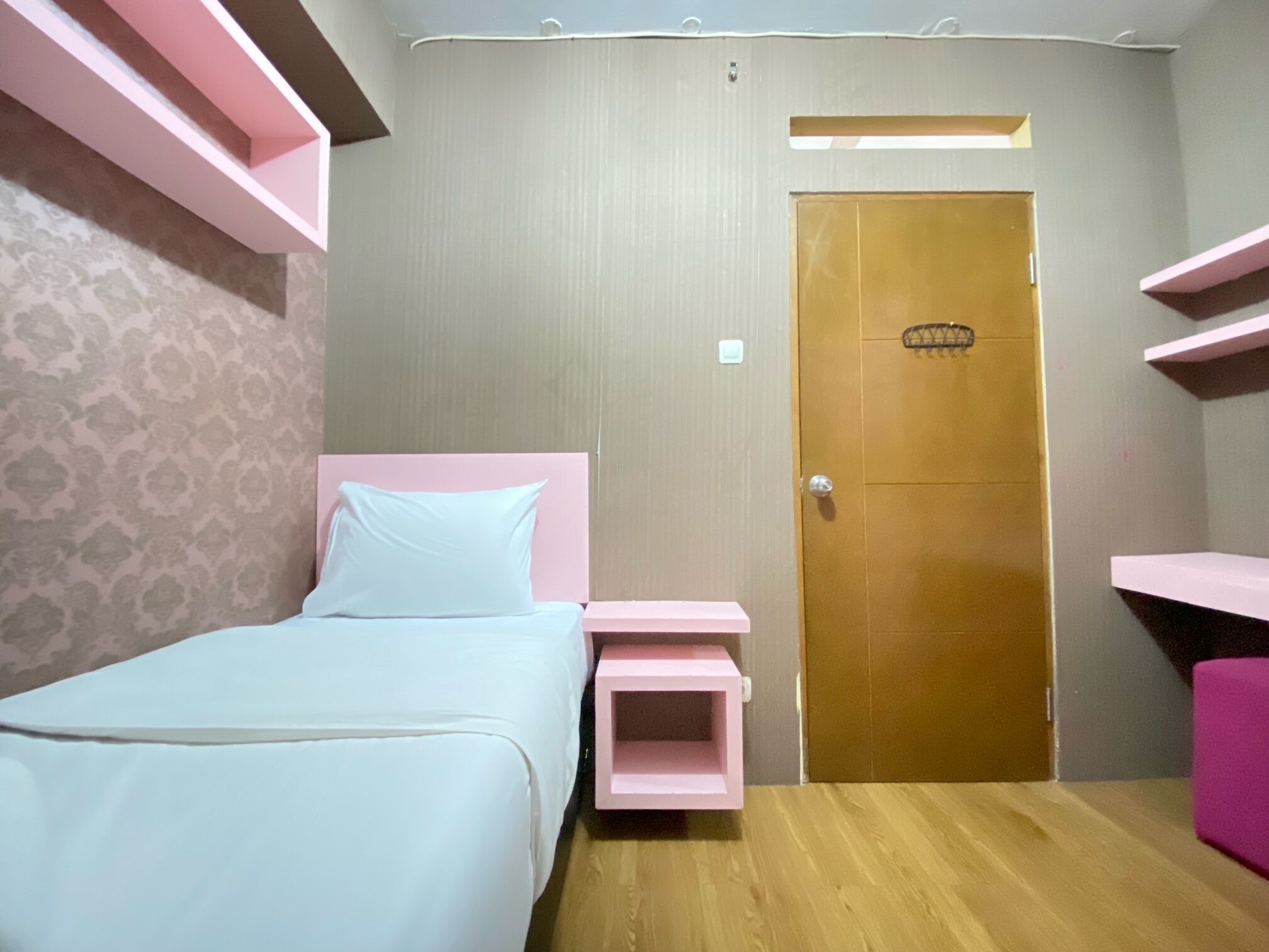 Un dormitorio con cama, puerta de madera y estanterías rosas.