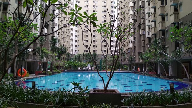 A swimming pool surrounded by greenery and tall residential buildings. - Spacious 3Br At Gateway Ahmad Yani Cicadas Apartment (Bandung)