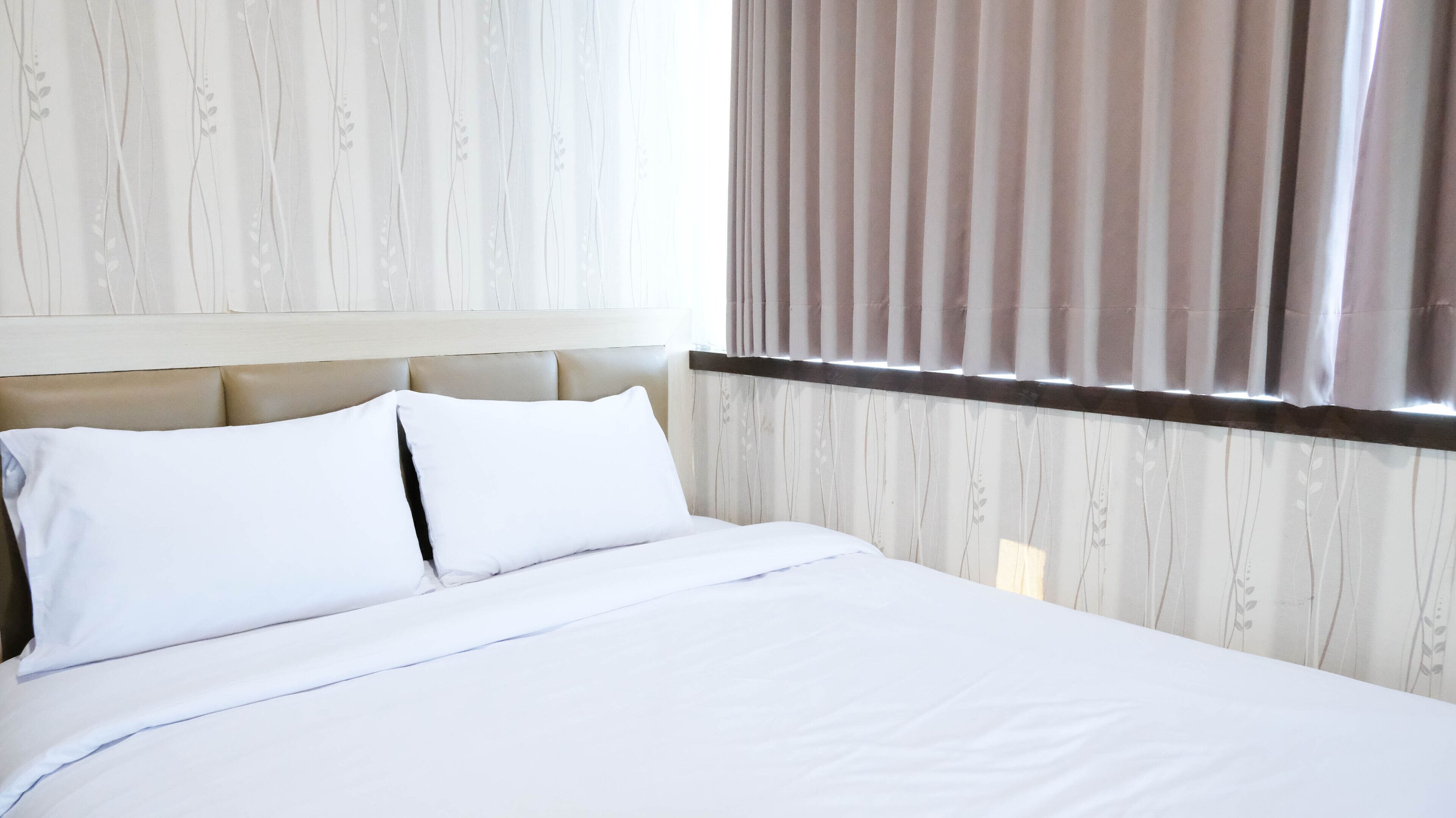 Une chambre d’hôtel avec un lit, du linge de lit blanc, une tête de lit et une fenêtre avec des rideaux.