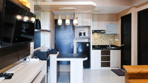 A compact kitchenette with a flat-screen TV, a microwave, and a refrigerator. - Best View And Cozy Living 2Br At Tamansari Papilio Apartment (Surabaya)