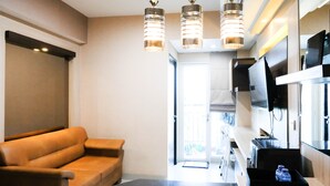 A modern living room with a leather sofa, a flat-screen TV mounted on the wall, and a kitchen area with a countertop and cabinets. - Best View And Cozy Living 2Br At Tamansari Papilio Apartment (Surabaya)