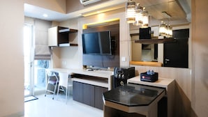 A modern kitchen with a flat-screen TV, a coffee machine, and a water dispenser. There is a dining area with a chair and a table. - Best View And Cozy Living 2Br At Tamansari Papilio Apartment (Surabaya)