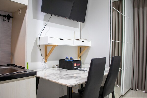 A modern hotel room with a marble countertop, a black chair, a small black table, a mounted TV, and a minibar. - Scenic And Comfortable Studio At West Vista Apartment (Jakarta)