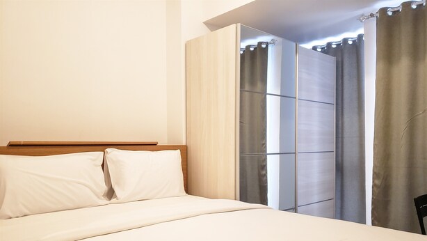 A neatly made bed with white linens and pillows, a wooden headboard, and a view of a bathroom with a shower curtain and a towel hanging on the wall.