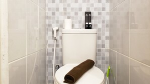 A bathroom with a toilet, a towel, a hand dryer, and a toilet brush.
