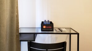 A small glass table with a black chair, a black bag labeled 'travelio' with water bottles, and a remote control.