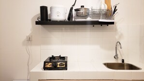 A kitchen with a stove, sink, and a shelf holding a rice cooker, a pot, and utensils.