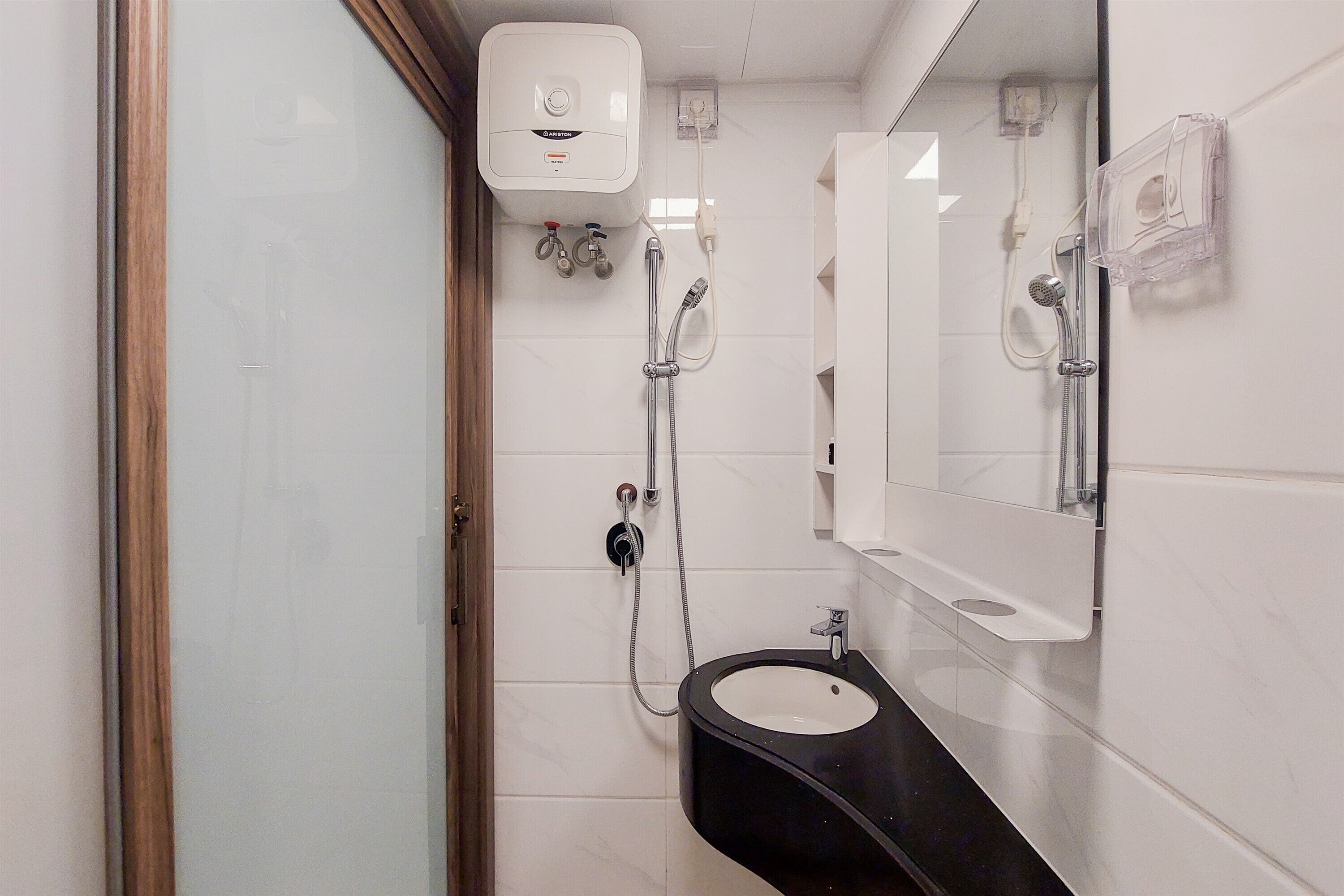 Ein modernes Badezimmer mit einem schwarzen Waschbecken, weißen Fliesen, einer Duschkabine aus Glas und einem angebrachten Spiegel.