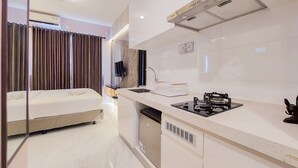 A modern hotel room with a bed, a kitchenette, and a bathroom. - Scenic And Restful Studio Sky House Bsd Apartment (Pagedangan)