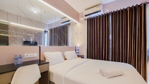 A hotel room with a bed, a desk, a chair, a mirror, and a window with curtains. - Scenic And Restful Studio Sky House Bsd Apartment (Pagedangan)