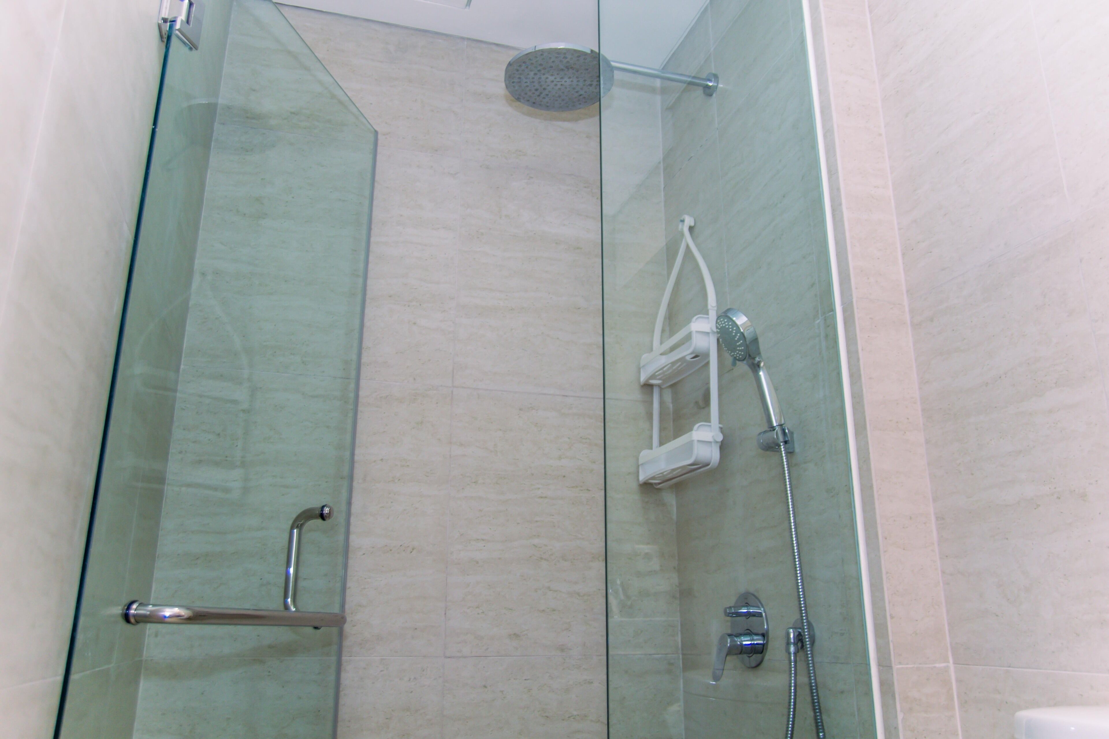 A glass-enclosed shower stall with a handheld showerhead, a wall-mounted faucet, and a handheld showerhead.