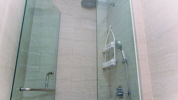 A glass-enclosed shower stall with a handheld showerhead, a wall-mounted faucet, and a handheld showerhead.