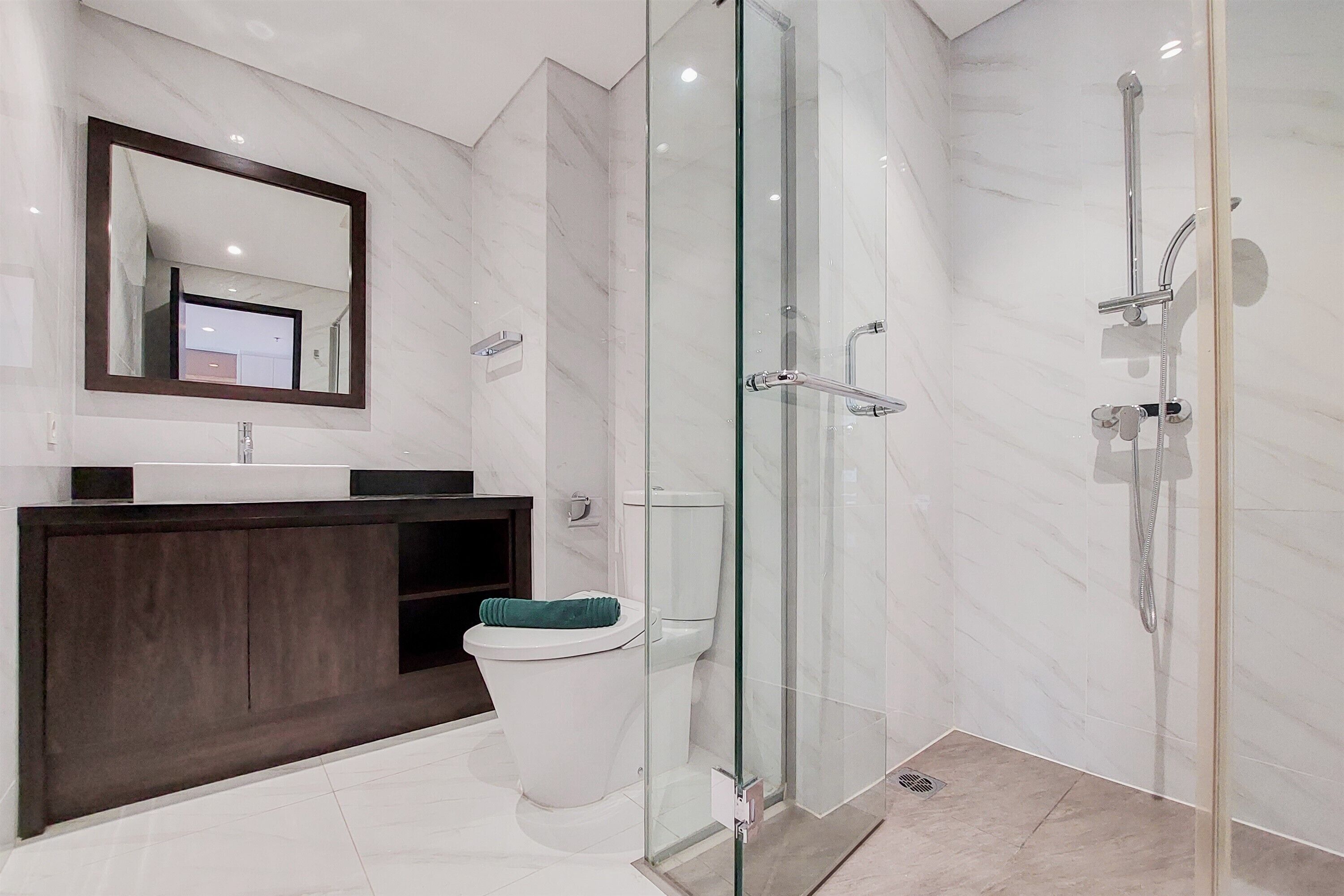 A modern bathroom with a glass-enclosed shower, a dark wood vanity, and a white toilet.