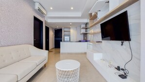 Un salon moderne avec un canapé blanc, une table basse ronde et un téléviseur à écran plat fixé au mur.