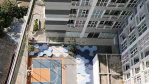 Vista aérea de un edificio de varios pisos con una cancha de baloncesto en primer plano, rodeado de vegetación y un camino pavimentado.