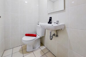 Bathroom features a white toilet, sink, and black bottle on a white tiled floor and walls.