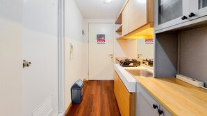 A narrow kitchen with wooden flooring, white cabinets, and a built-in microwave. - Comfortable Studio Apartment At M-Town Residence (Gading Serpong)