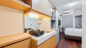 A modern hotel room with a wooden vanity, a built-in stove, a large mirror, a bed, and a small bedside table. - Comfortable Studio Apartment At M-Town Residence (Gading Serpong)