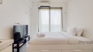 A hotel room with a bed, a TV on a stand, and a window with curtains.