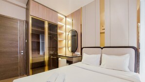 A hotel room with a large bed, a wardrobe, a vanity with a mirror, and a bedside table. - Scenic And Restful 2Br Sky House Bsd Apartment (Pagedangan)