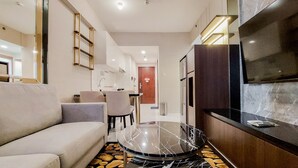 A modern living room with a sofa, a glass-top coffee table, and a TV mounted on the wall. - Scenic And Restful 2Br Sky House Bsd Apartment (Pagedangan)