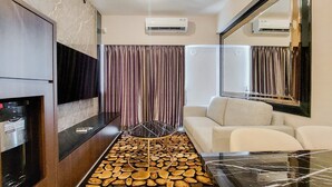 A hotel room with a marble wall, a white sofa, a coffee machine, and a unique wooden floor design. - Scenic And Restful 2Br Sky House Bsd Apartment (Pagedangan)