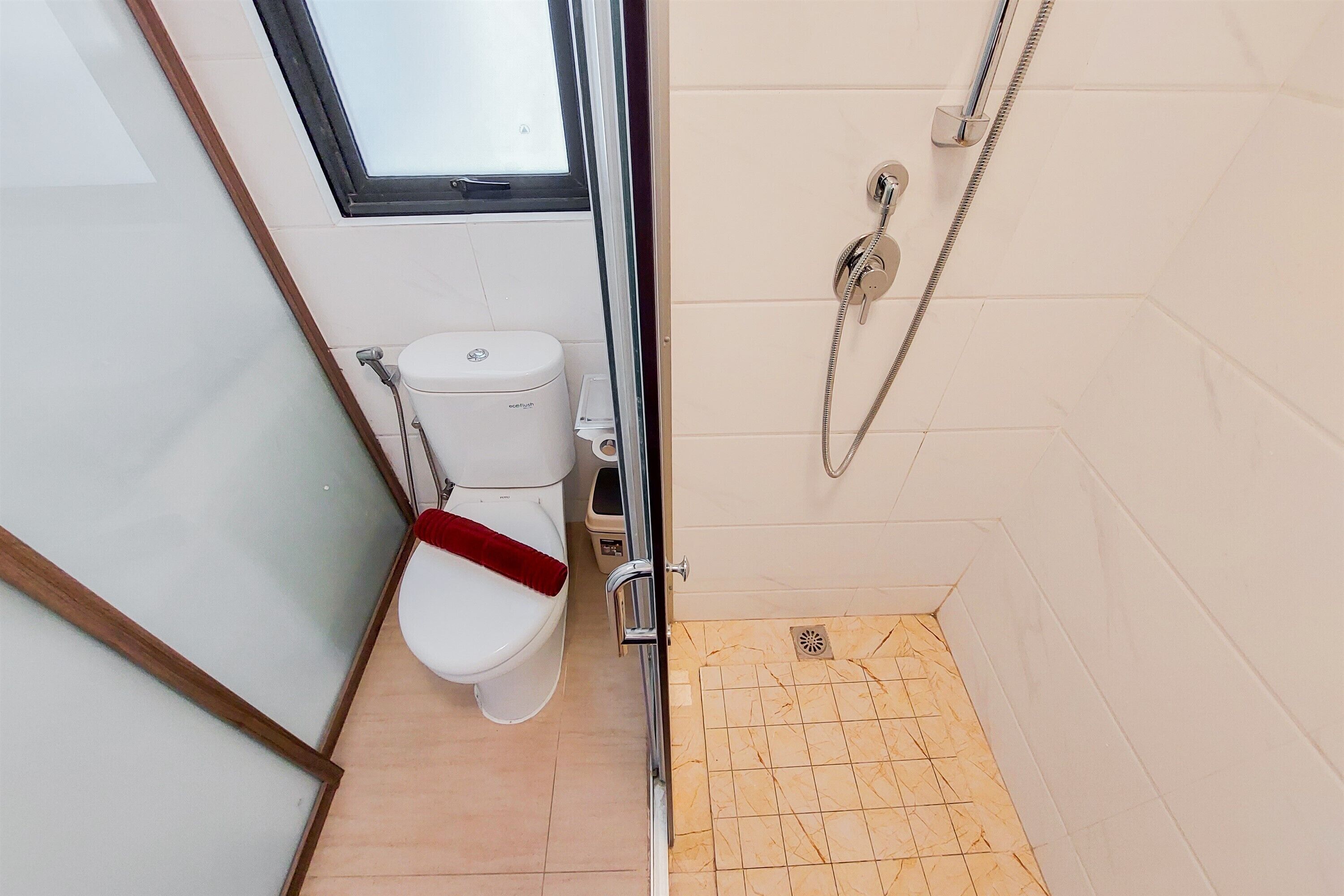 A small bathroom with a toilet, a shower, and a window.
