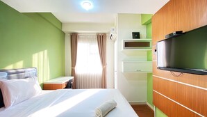 A hotel room with a bed, a desk, a television, and a window with curtains. - Warm Studio Apartment at Harvard Jatinangor (Cileunyi)