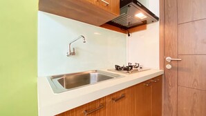 A compact kitchen with a stainless steel sink, a gas stove, wooden cabinets, and a white countertop. - Warm Studio Apartment at Harvard Jatinangor (Cileunyi)