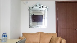 A room with a brown sofa, a small table with water bottles, and a mirror on the wall. - Warm And Cozy Studio At Cinere Resort Apartment (Depok)