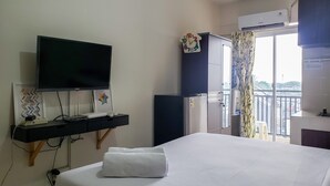 A hotel room with a bed, a TV, a desk with a computer, a wardrobe, and a window with a view. - Warm And Cozy Studio At Cinere Resort Apartment (Depok)