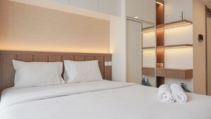 A modern hotel room with a large bed, wooden headboard, and built-in shelves with lighting. - Comfy And Warm Studio Room At Sky House Bsd Apartment (Pagedangan)
