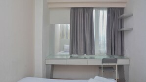 A hotel room with a bed, a glass desk with a chair, a mirror, and a window with curtains. - Minimalist And Warm 2Br At Bassura City Apartment (Jakarta)