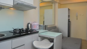 A compact kitchen with a gas stove, a kettle, and a microwave. There is a small dining area with a chair and a table. - Minimalist And Warm 2Br At Bassura City Apartment (Jakarta)