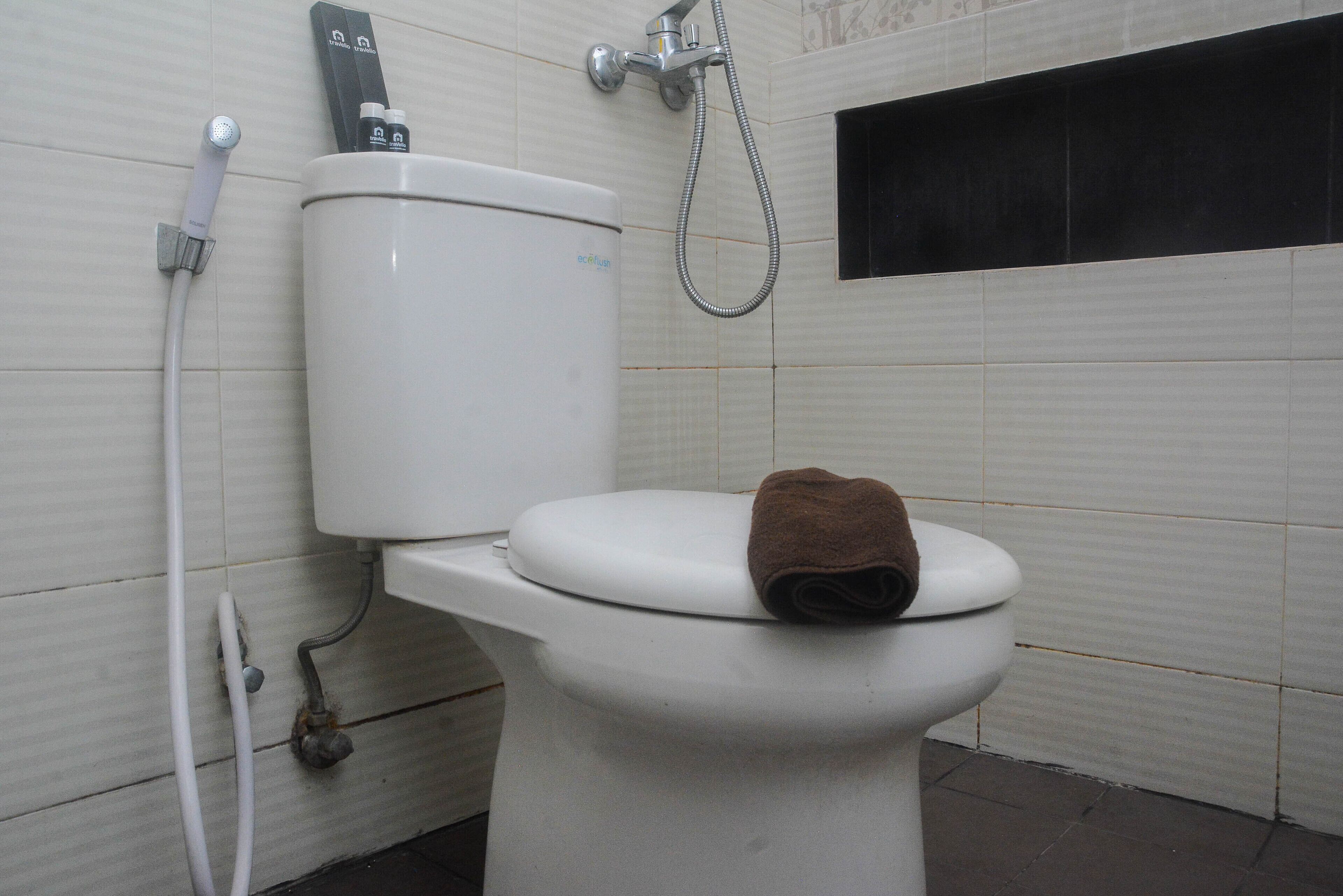 A toilet with a towel on the seat, a shower head, and a toilet paper holder.