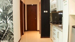 A narrow hallway leading to a closed door, with a kitchen area on the right featuring white cabinets and stainless steel appliances. - Great Location And Comfy 2Br Apartment At Thamrin Residence (Jakarta)