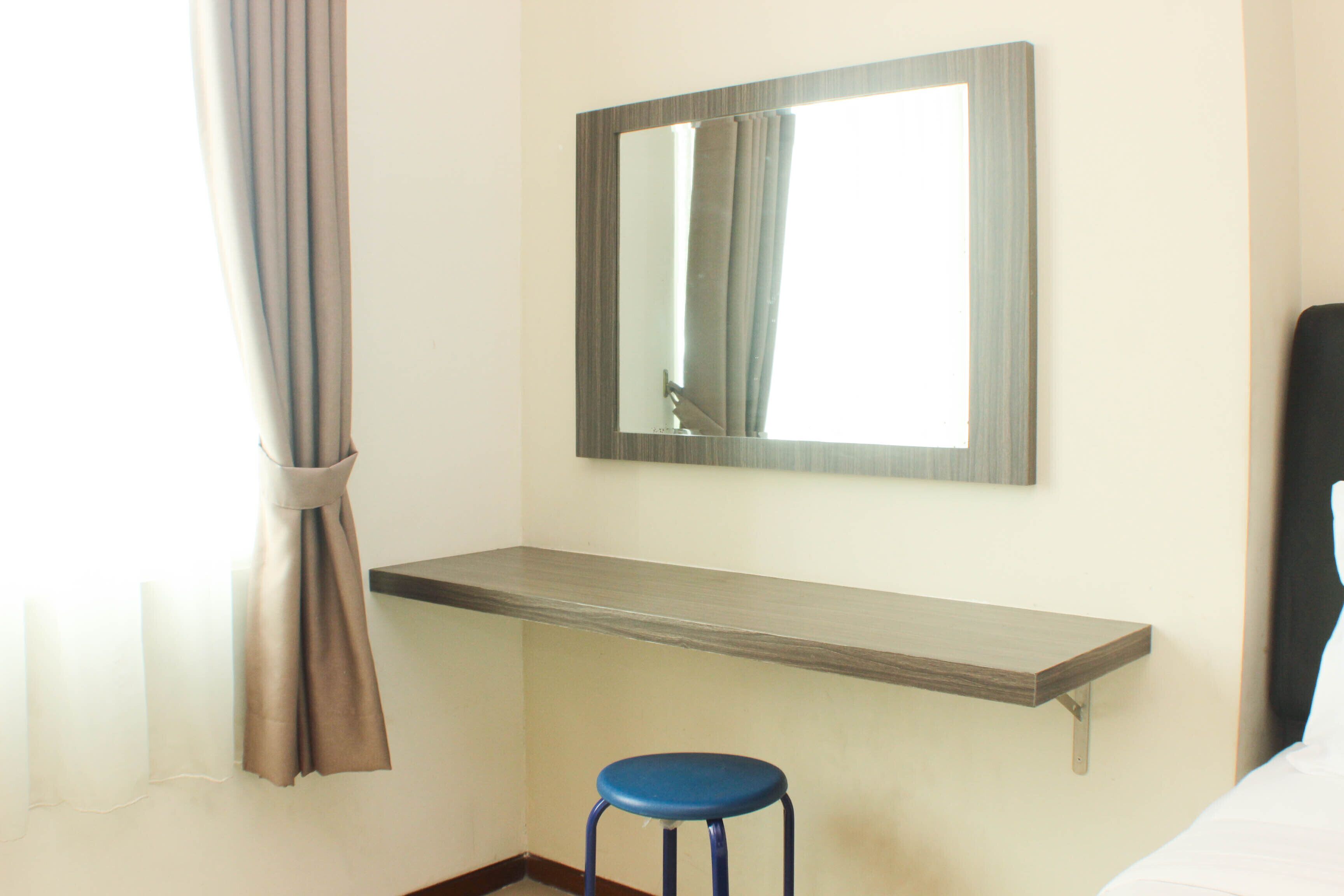 A hotel room with a bed, a blue stool, a mirror, and a window with curtains.