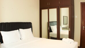 A neatly made bed with white linens, a dark headboard, and a set of wooden doors with a mirror. - Great Location And Comfy 2Br Apartment At Thamrin Residence (Jakarta)