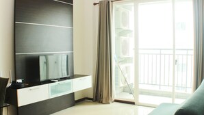 A modern living room with a flat-screen TV, a sofa, and a sliding glass door to a balcony. - Great Location And Comfy 2Br Apartment At Thamrin Residence (Jakarta)
