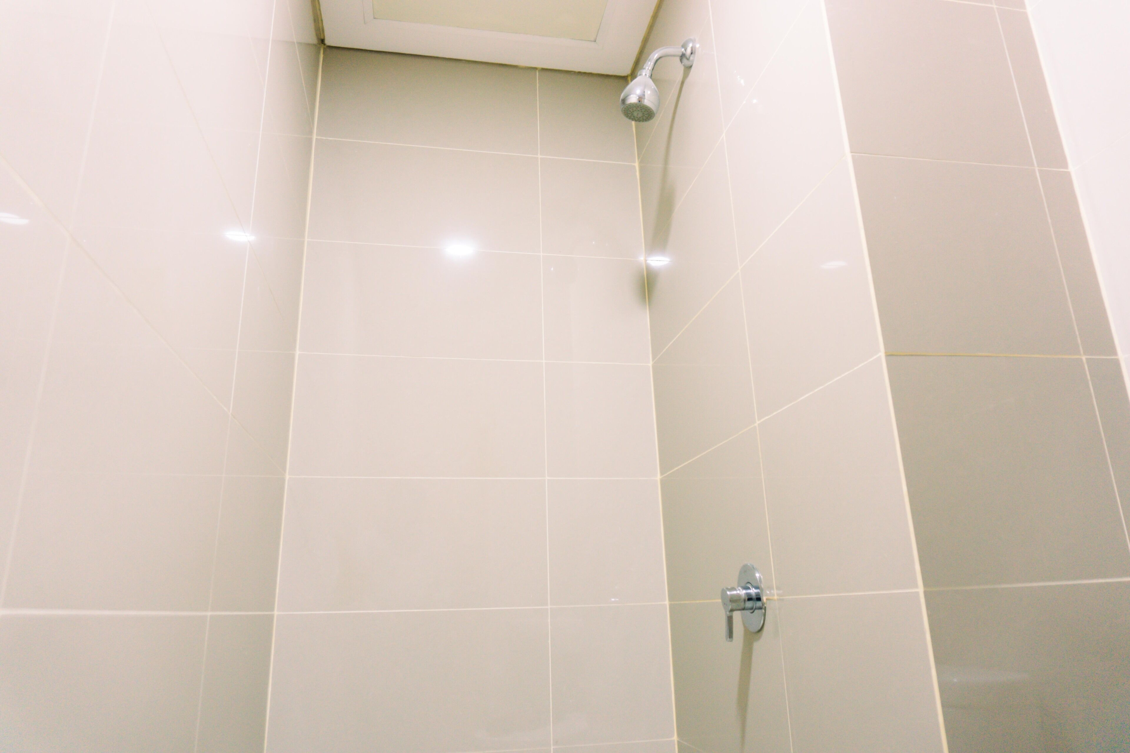 A bathroom with white tiles, a showerhead, and a faucet.